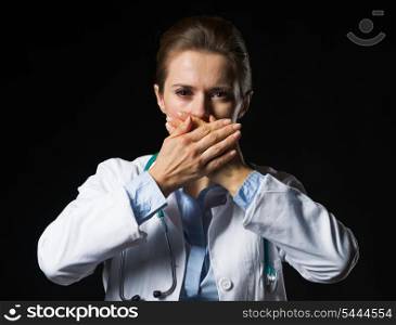 Portrait of doctor woman showing speak no evil gesture isolated on black