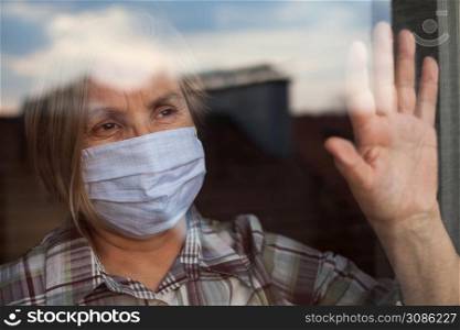 Portrait of elderly senior citizen wearing face mask looking through room window,Coronavirus COVID-19 pandemic outbreak nursing home crisis,high mortality rate and death cases among older population