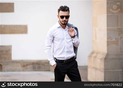 Portrait of elegant and fashionable man in black sunglasses posing on the street