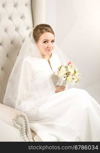 Portrait of elegant bride with white roses sitting on chair at studio