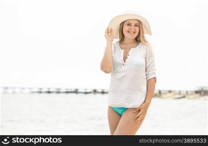 Portrait of elegant brunette woman in white hat posing against seashore