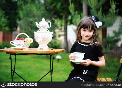 Portrait of elegant child girl in a black dress having a tea party outdoors