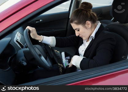 Portrait of elegant woman driving car and looking inside handbag