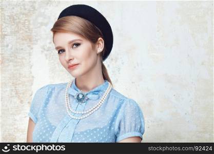 Portrait of elegant young woman wearing blue blouse, pearl necklace and beret on grunge background