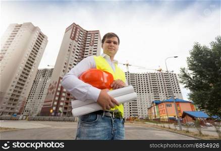 Portrait of engineer standing at new buildings with blueprints