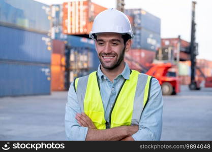 Portrait of engineer worker of factory technician stand with happy emotion and in front of cargo container crane in workplace area. Concept of good support best successful for industrial business.