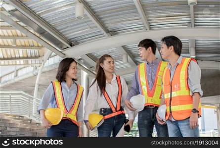 Portrait of engineering group wearing uniforms and holding safety helmets while standing outside near buildings. Construction Concept.