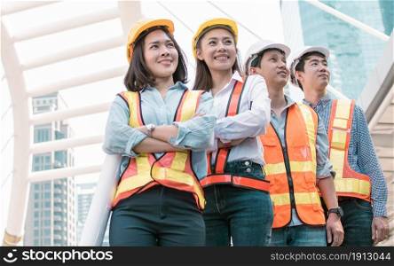 Portrait of engineering group wearing uniforms and holding safety helmets while standing outside near buildings. Construction Concept.