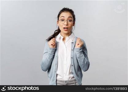 Portrait of excited and tempting cute asian girl in glasses, awaiting with thrill and interest for new season of favorite tv show coming up, looking ancitipation and amusement, stand grey background.. Portrait of excited and tempting cute asian girl in glasses, awaiting with thrill and interest for new season of favorite tv show coming up, looking ancitipation and amusement, stand grey background