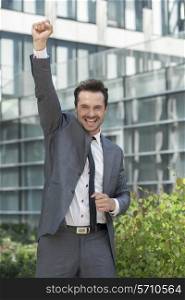 Portrait of excited businessman with arm raised celebrating success outside office building