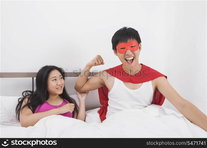 Portrait of excited man in superhero costume with woman on bed