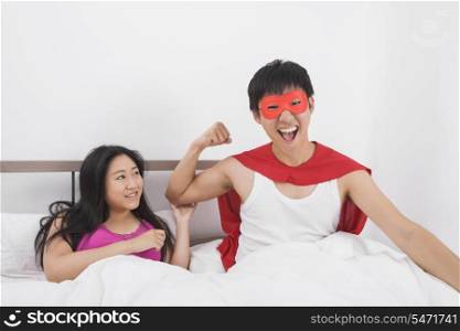 Portrait of excited man in superhero costume with woman on bed