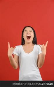 Portrait of Excited young asian woman in white t-shirt doing rock symbol with hands up isolated on red background. Expression and lifestyle concept.