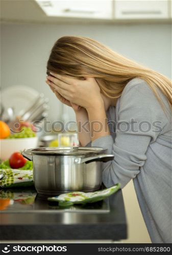 Portrait of exhausted young housewife posing on kitchen while cooking soup