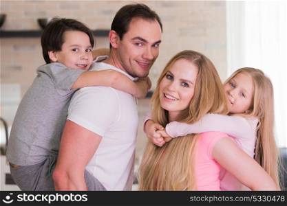 Portrait of family at home. Portrait of happy family, father and mother giving boy and girl piggy back ride at home