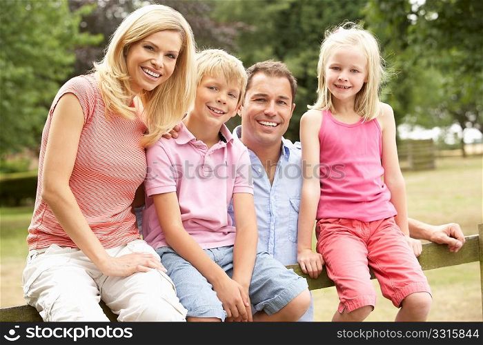 Portrait Of Family Sitting On Fence In Countryside