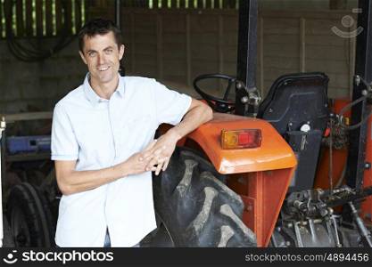 Portrait Of Farmer Standing In Barn With Tractor