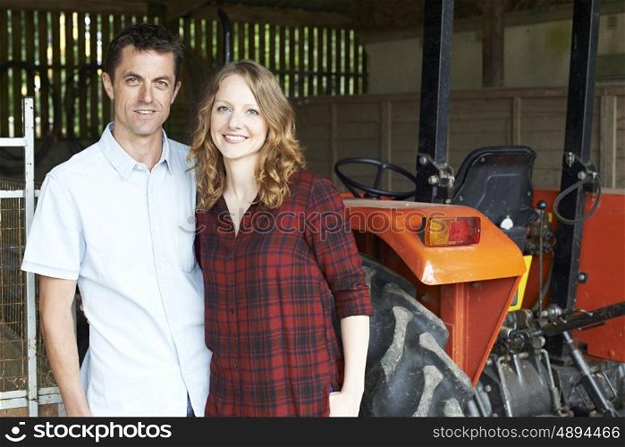 Portrait Of Farmers Standing In Barn With Tractor