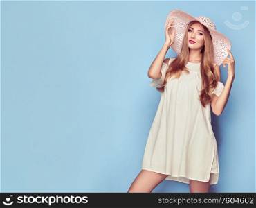 Portrait of Fashion Young woman in Pink Dress. Lady in Stylish Summer Outfit. Girl Posing on a Blue Background in Pink Hat. Stylish Hairstyle. Spring collection casual clothes