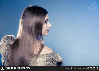 Portrait of fashionable girl with long hair. Young woman in fur coat on blue. Studio shot. Winter fashion.