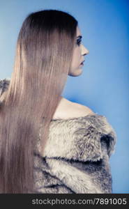 Portrait of fashionable girl with long hair. Young woman in fur coat on blue. Studio shot. Winter fashion.