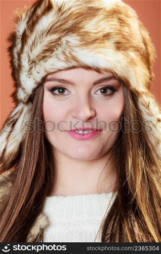 Portrait of fashionable pretty woman in fur winter cap hat on orange background in studio.. Girl in fur cap