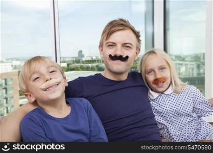 Portrait of father and children with artificial mustache at home