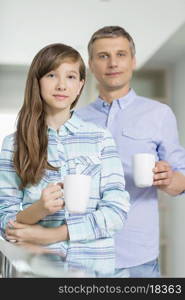 Portrait of father and daughter holding coffee cups at home