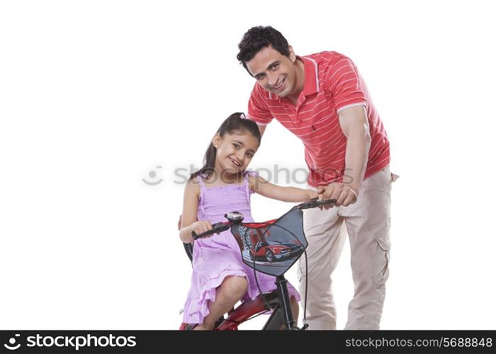 Portrait of father assisting daughter in riding bicycle against white background