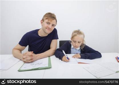 Portrait of father sitting with daughter studying at table
