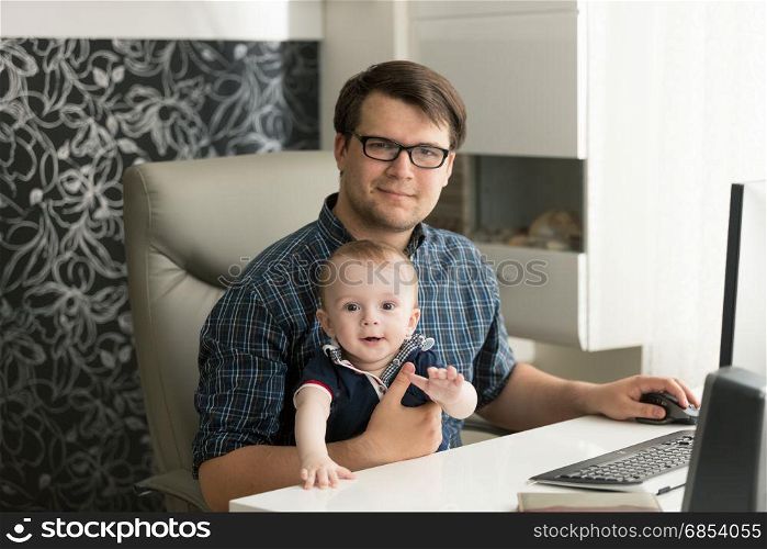 Portrait of father sitting with his little son and working at home
