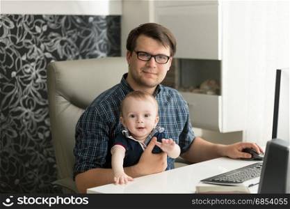 Portrait of father sitting with his little son and working at home