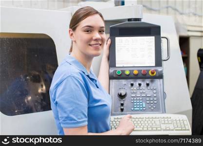 Portrait Of Female Apprentice Engineer Operating CNC Machine In Factory