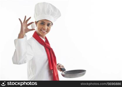 Portrait of female chef holding an egg and frying pan isolated over white background