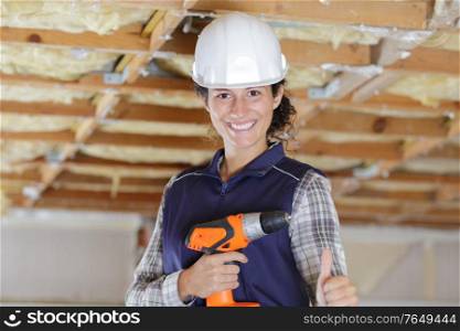portrait of female construction worker holding drill with thumbs up