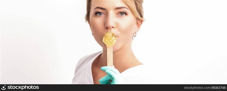 Portrait of female cosmetologist holds a wooden stick with a wax covering her lips on white background. Cosmetologist holds wooden stick with wax
