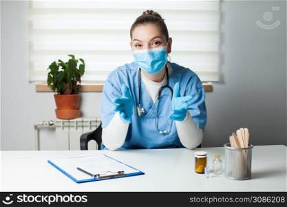Portrait of female doctor wearing protective gloves and face mask,talking online with patient,young GP woman in blue uniform consulting person online,remote televisit assistance,telemedicine concept