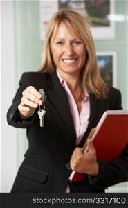 Portrait Of Female Estate Agent In Office Handing Over Keys