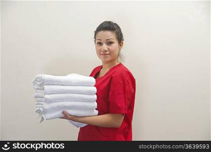 Portrait of female housekeeper holding clean white towels against gray background