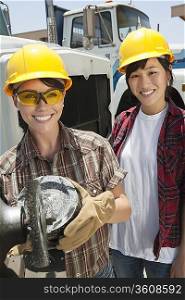Portrait of female industrial worker buffing a truck engine cylinder with coworker standing besides her