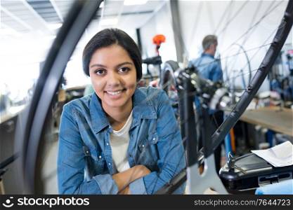 portrait of female mechanic seen through spokes of bicycle wheel