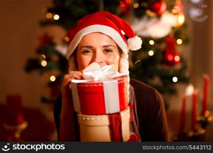 Portrait of female near Christmas tree hiding behind pile of present boxes &#xA;