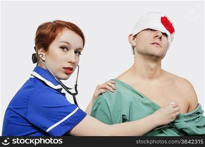 Portrait of female nurse treating an injured male patient against gray background