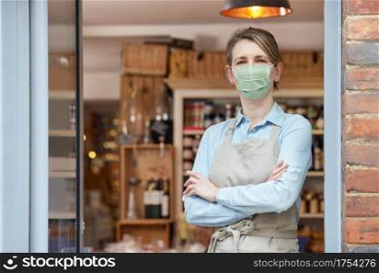 Portrait Of Female Owner Standing Outside Delicatessen Wearing Face Mask During Health Pandemic