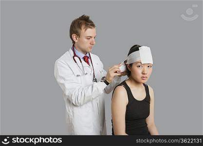 Portrait of female patient with doctor wrapping bandage to her head
