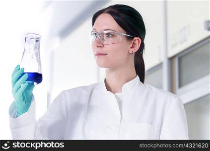 Portrait of female scientist examining glass container