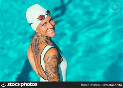 Portrait of female swimmer with tattoos posing by the pool