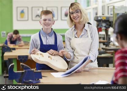 Portrait Of Female Teacher Helping Male High School Student Building Guitar In Woodwork Lesson