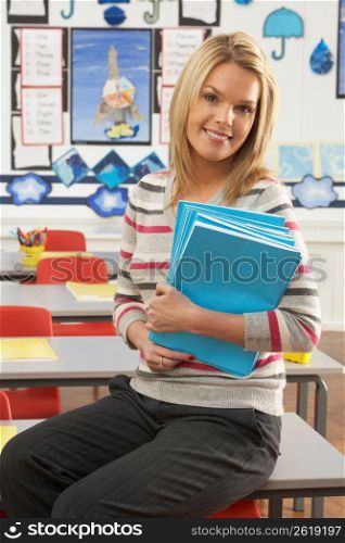 Portrait Of Female Teacher Sitting At Desk In Classroom