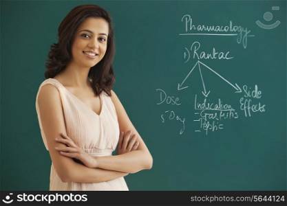 Portrait of female teacher with arms crossed standing against green board